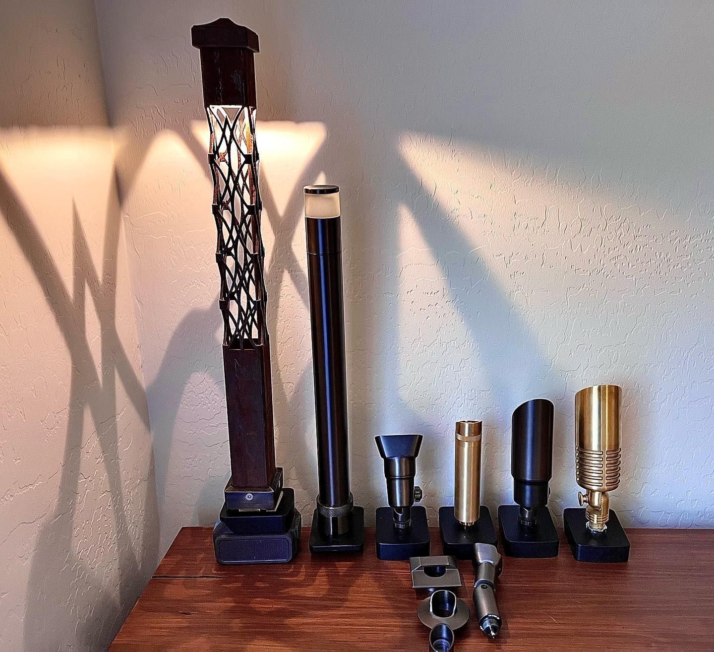 Assorted black, silver, and brass flashlights arranged on a wooden table against a wall.