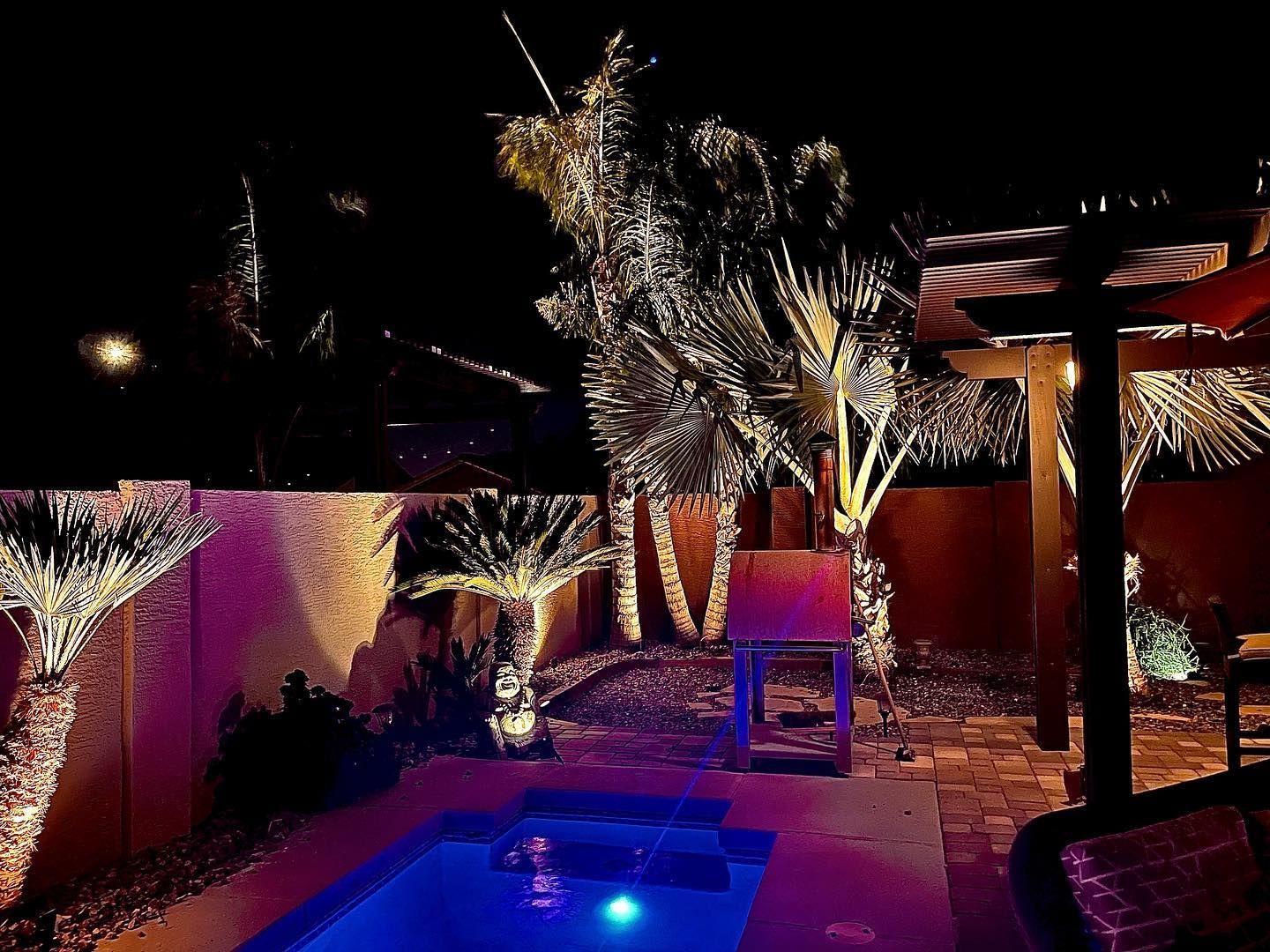 Nighttime patio with lit palm trees, a glowing pool, and a torii-style gate in the background