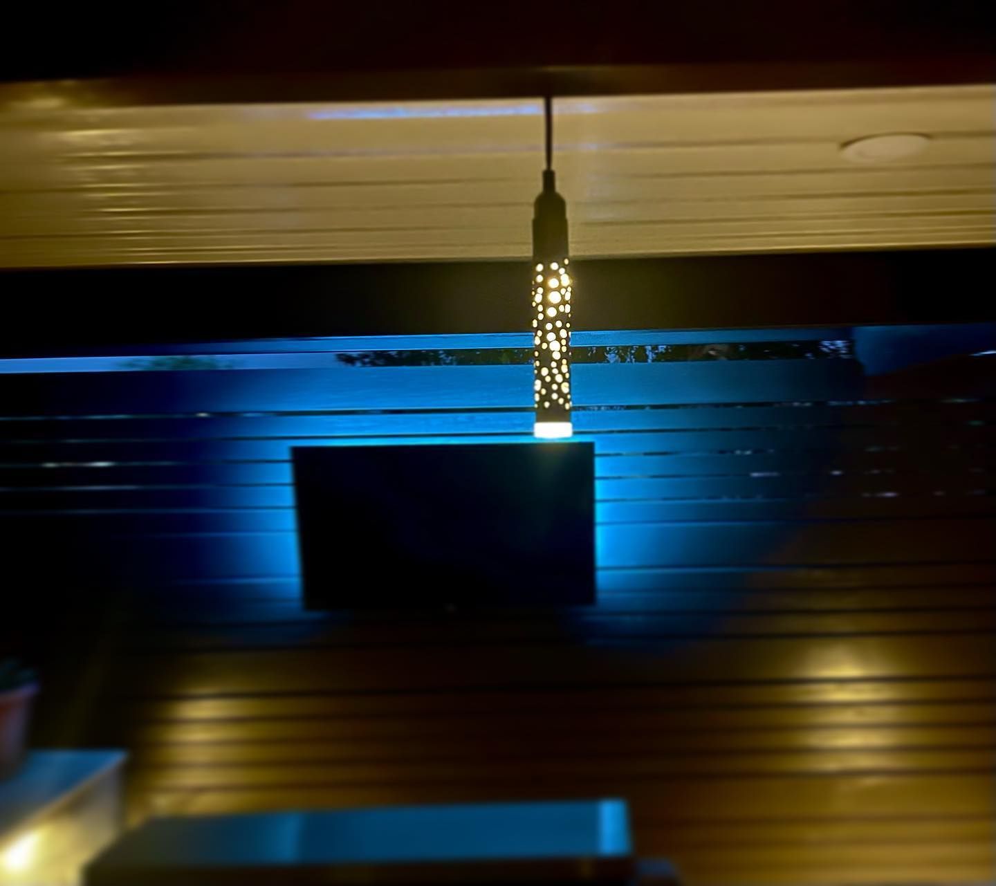 Dimly lit indoor scene with a glowing pendant light above a dark rectangular wall feature and blue accent lighting