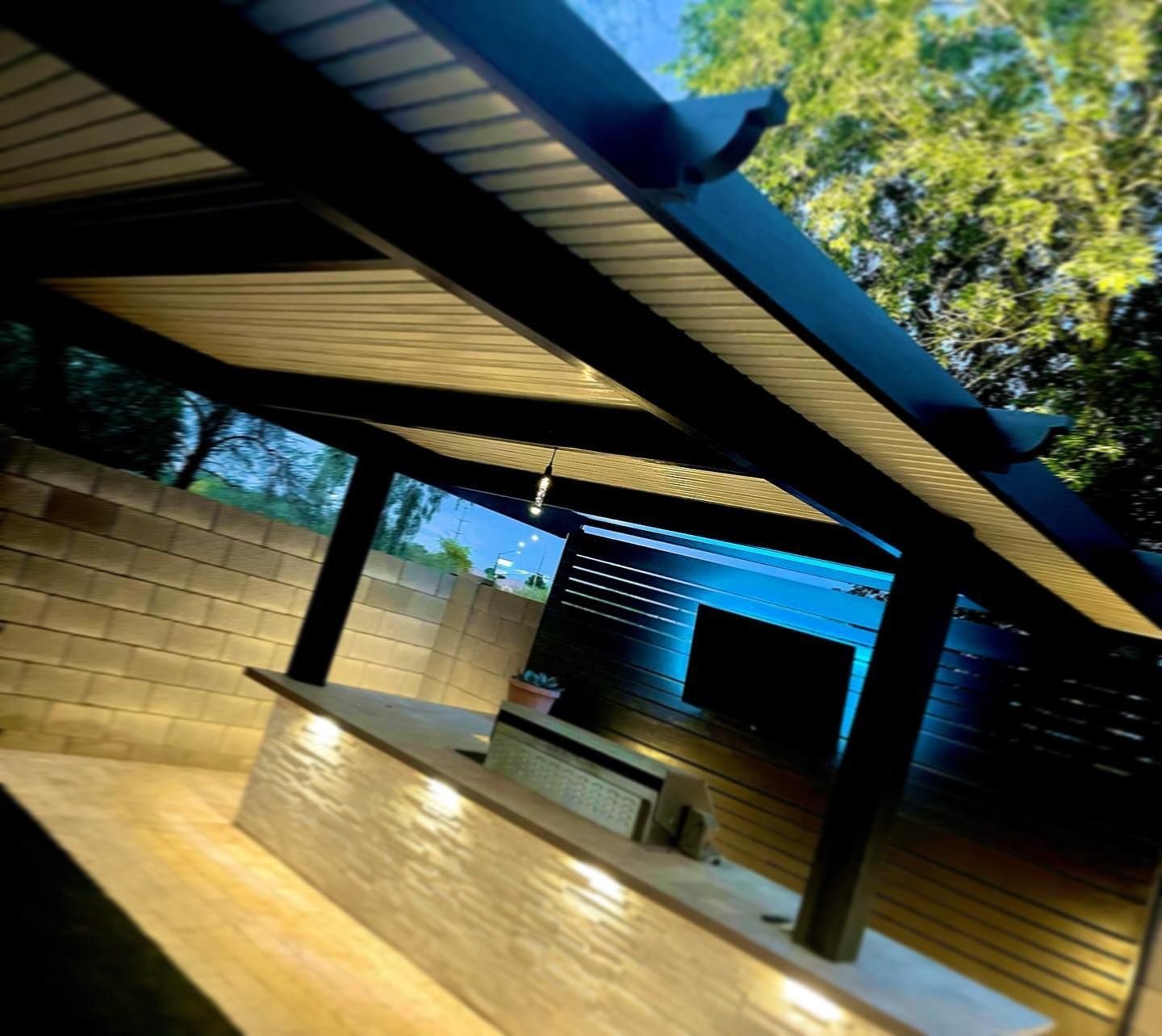 Covered outdoor patio with brick counter, black posts, and slanted roof in a wooded yard