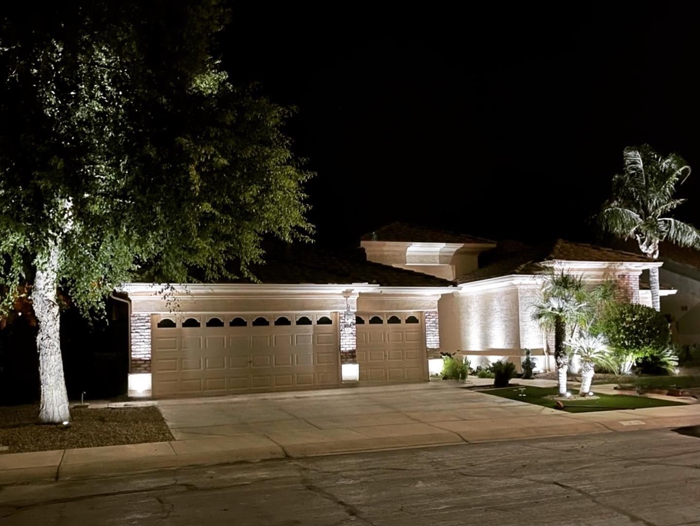 Single-story suburban house at night, warmly lit with trees and a garage in front.