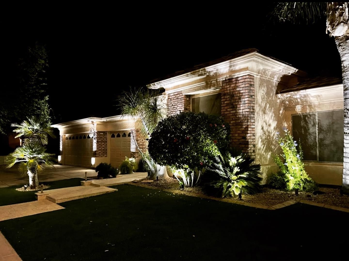 Well-lit modern house at night with landscaped front yard and glowing exterior lights