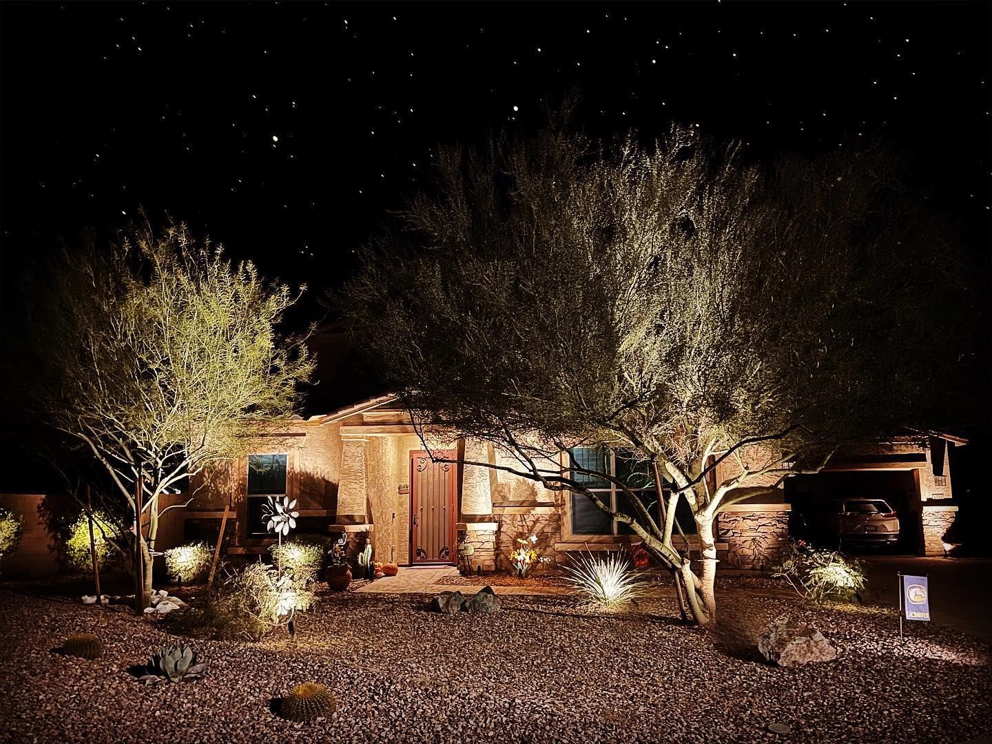 Desert house lit at night, with trees and a starry sky.