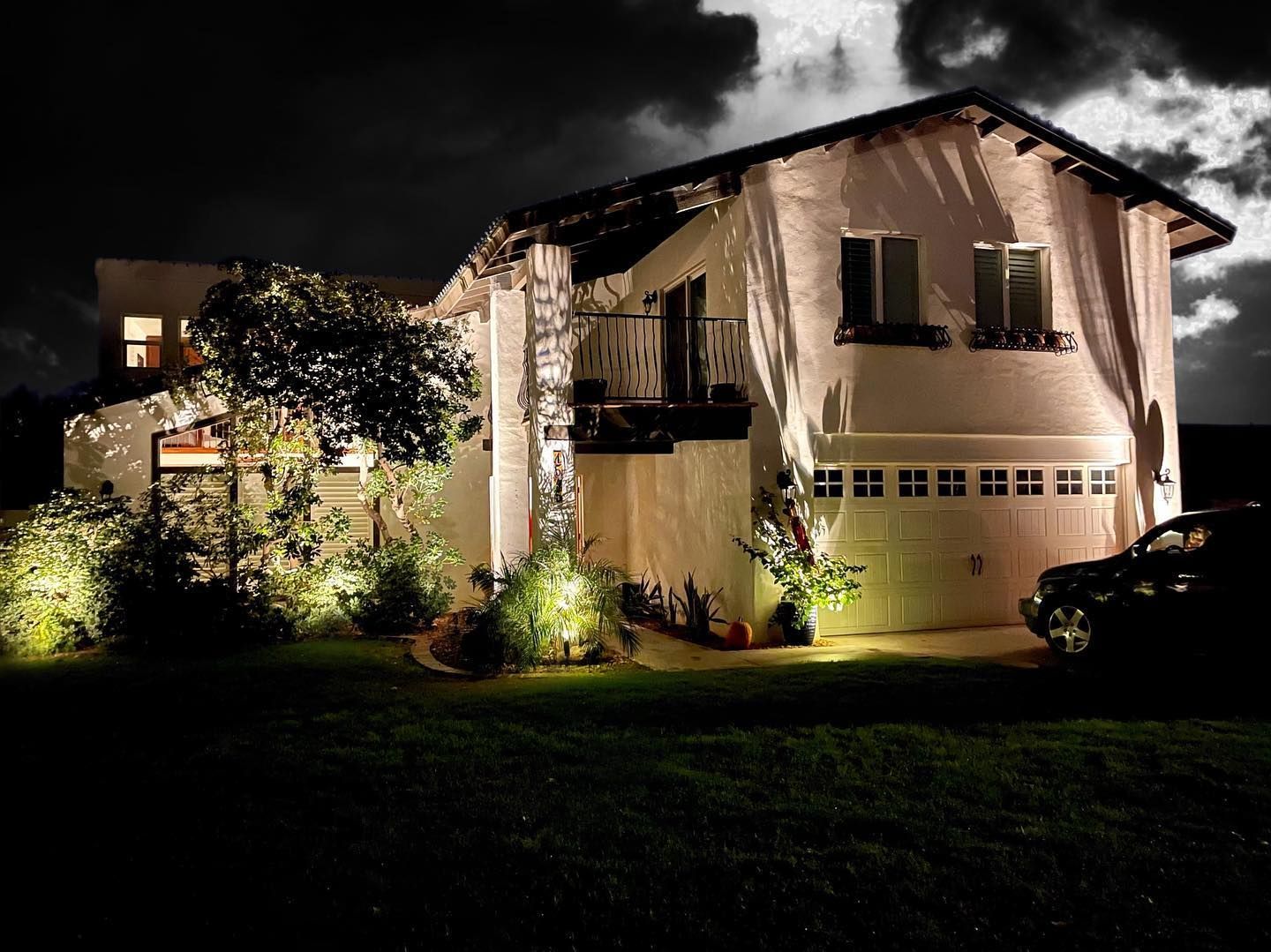 Illuminated two-story house at night with dark clouds overhead and a car parked in the driveway