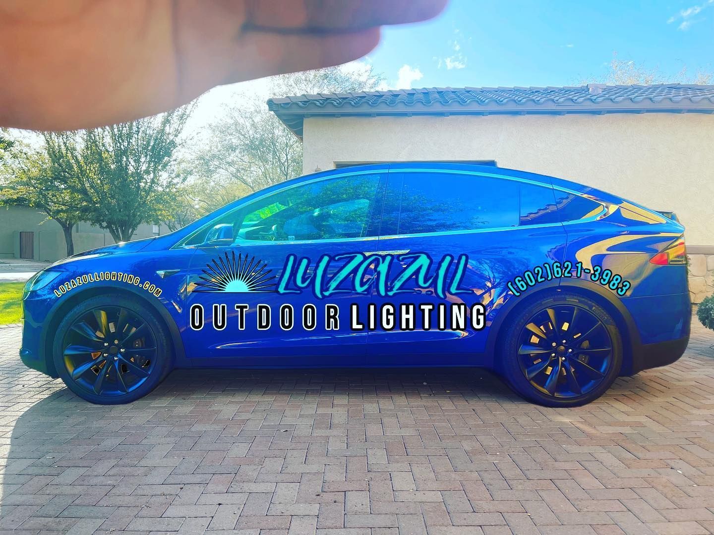 Blue car with “Arizona Outdoor Lighting” wrap parked on a brick driveway at sunset