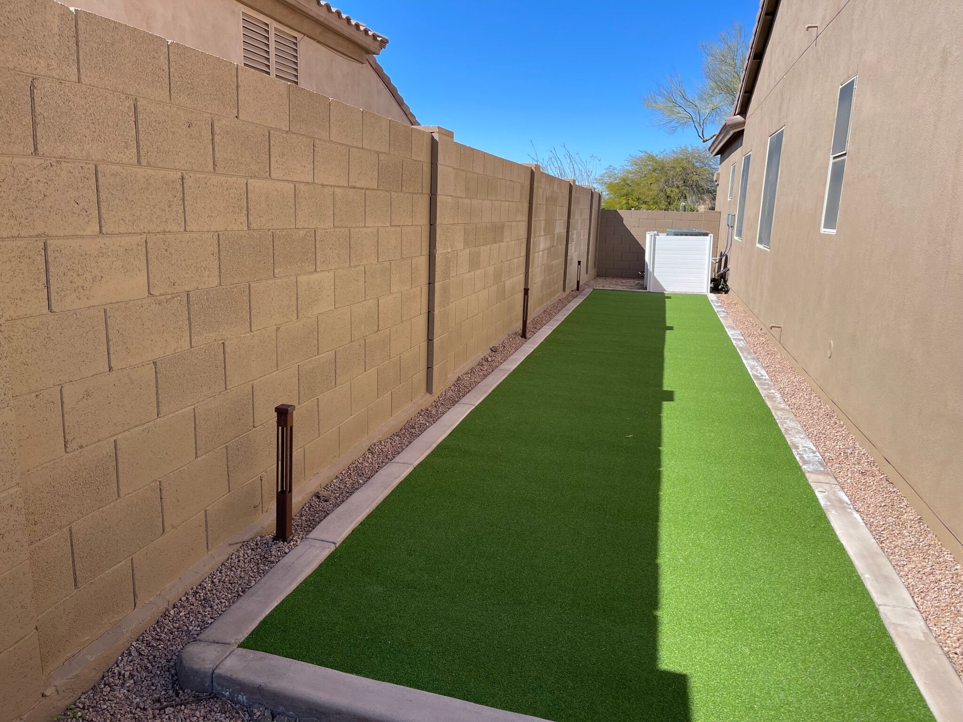 Narrow backyard side yard with green artificial turf between tan block walls leading to a gate