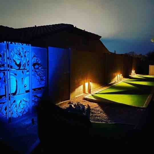 Nighttime outdoor walkway with blue-lit wall art and warm ground lights along a modern building