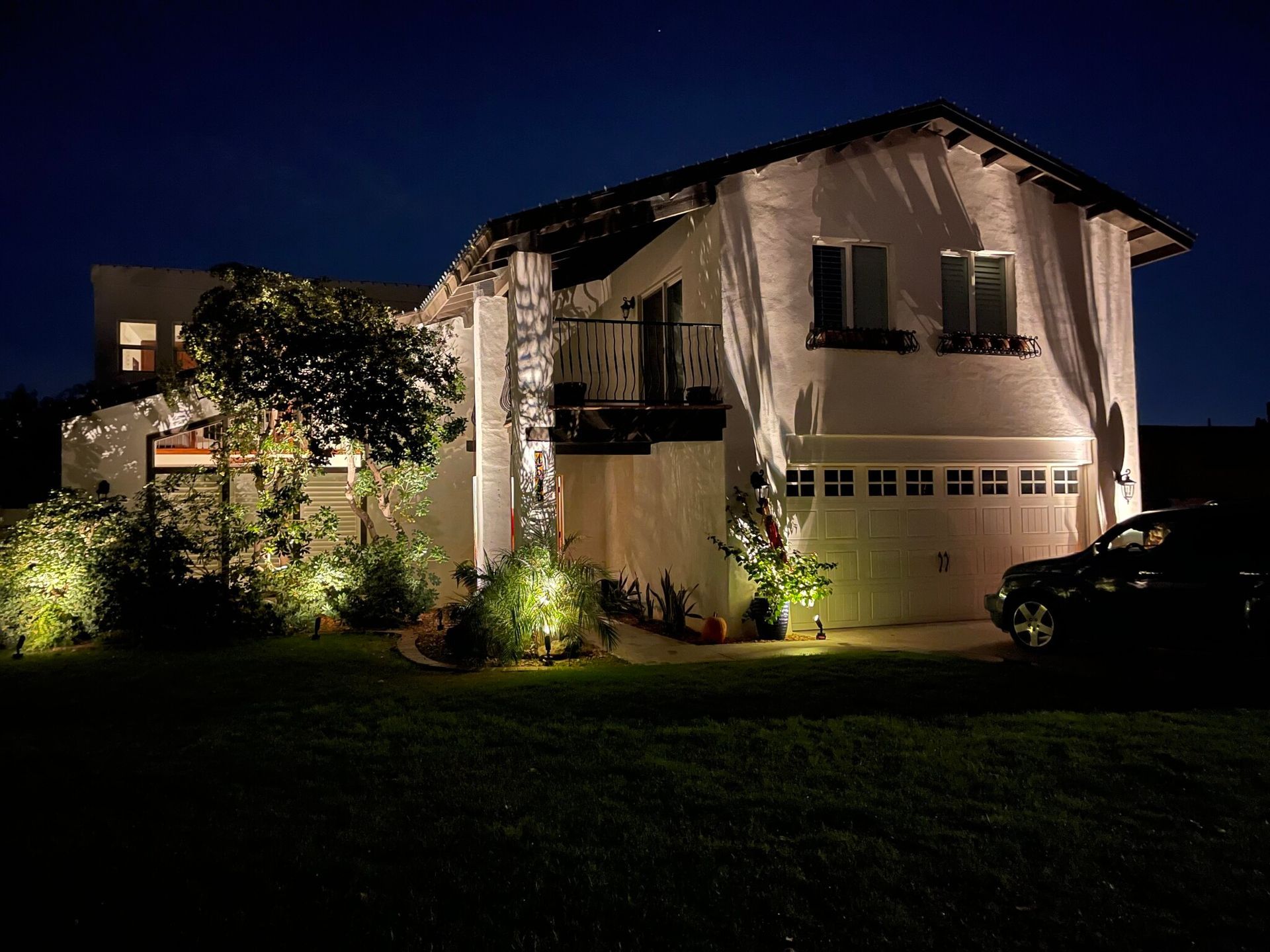 Well-lit two-story house at night with a garage, trees, and a dark front lawn