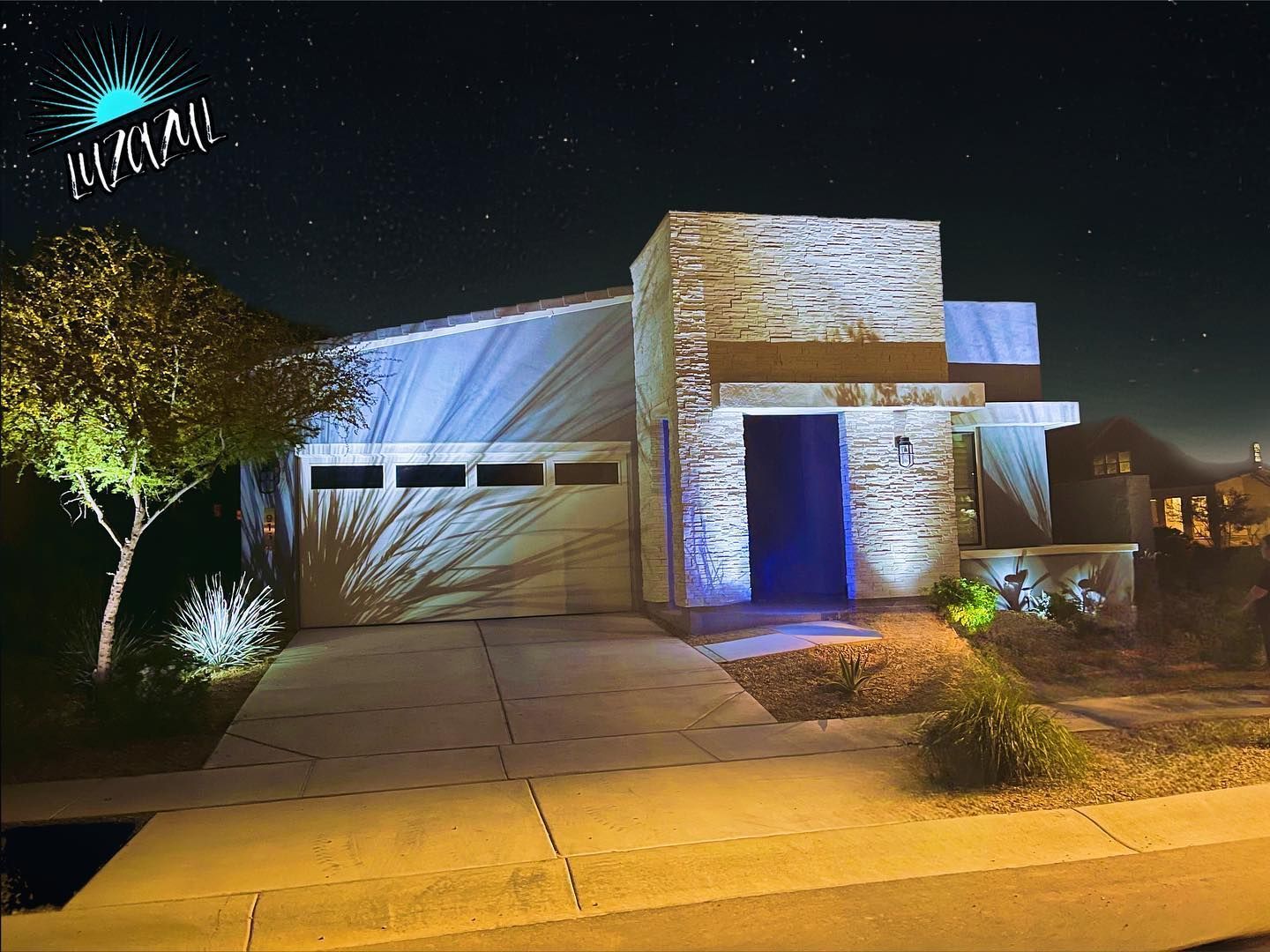 Modern house at night with lit exterior and driveway under a starry sky
