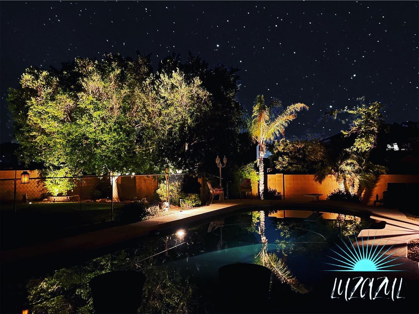 Nighttime backyard with lit trees, a swimming pool, and warm reflections under a starry sky