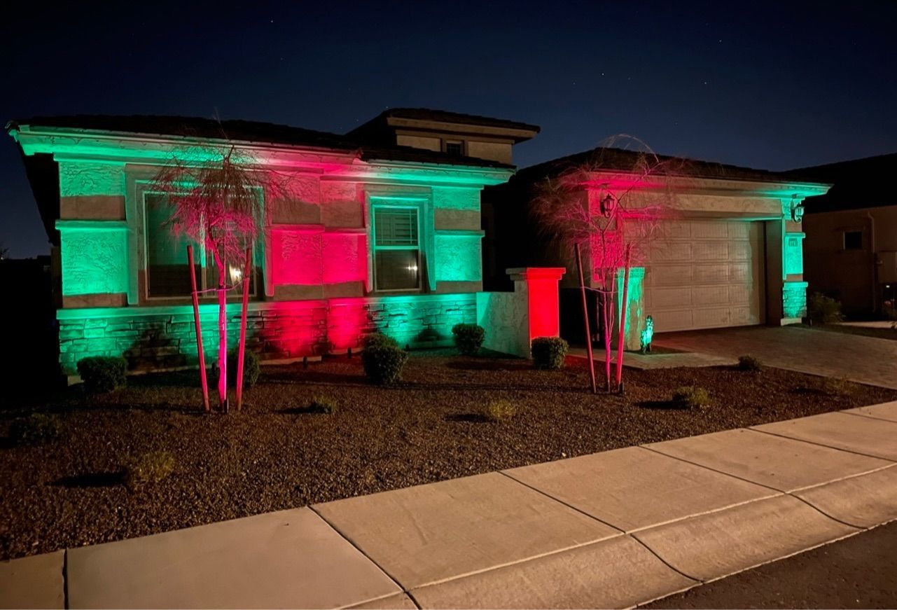 Single-story house lit with pink and teal lights at night, with a sidewalk in front