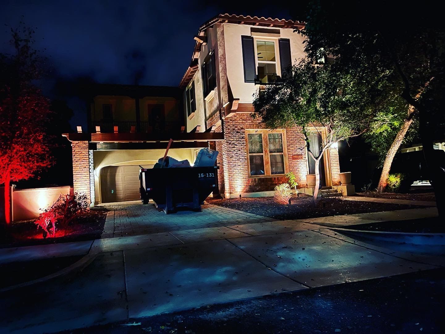 Suburban house at night with brick facade, lit windows, driveway, and a blue truck in front