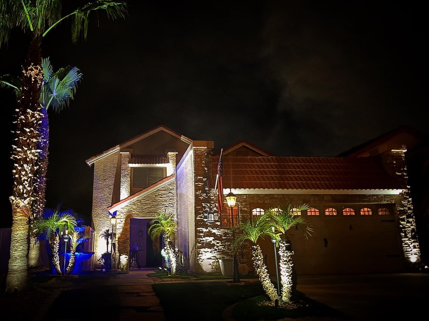House exterior at night with palm trees and colorful holiday lights illuminating the facade