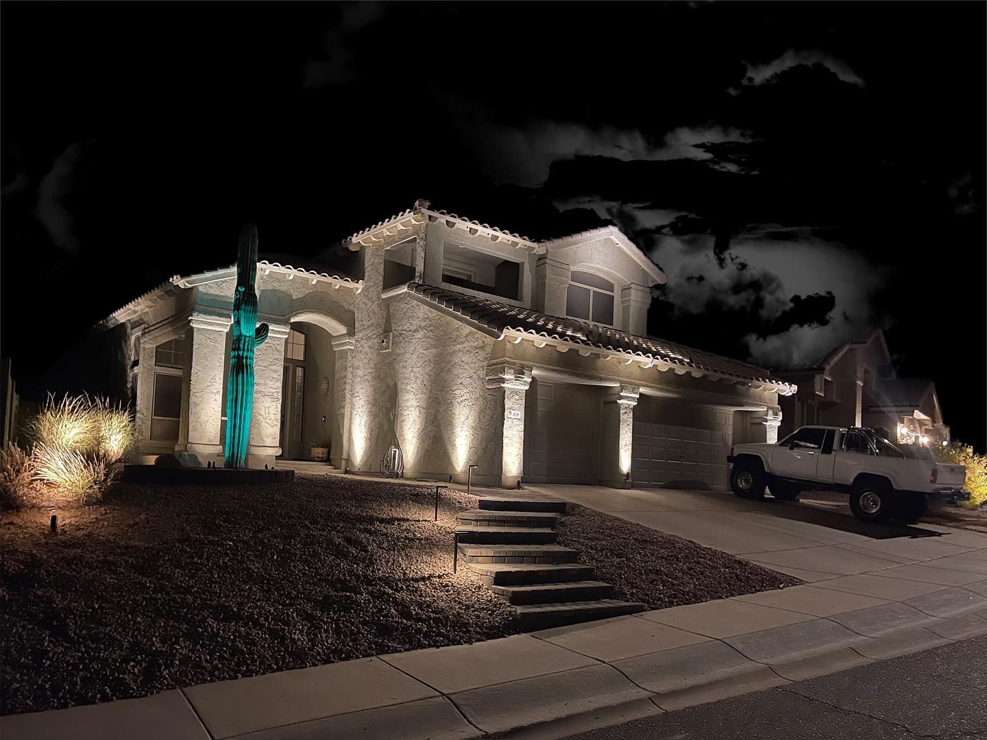Lit stone house at night with a lit turquoise fountain and parked white pickup in the driveway