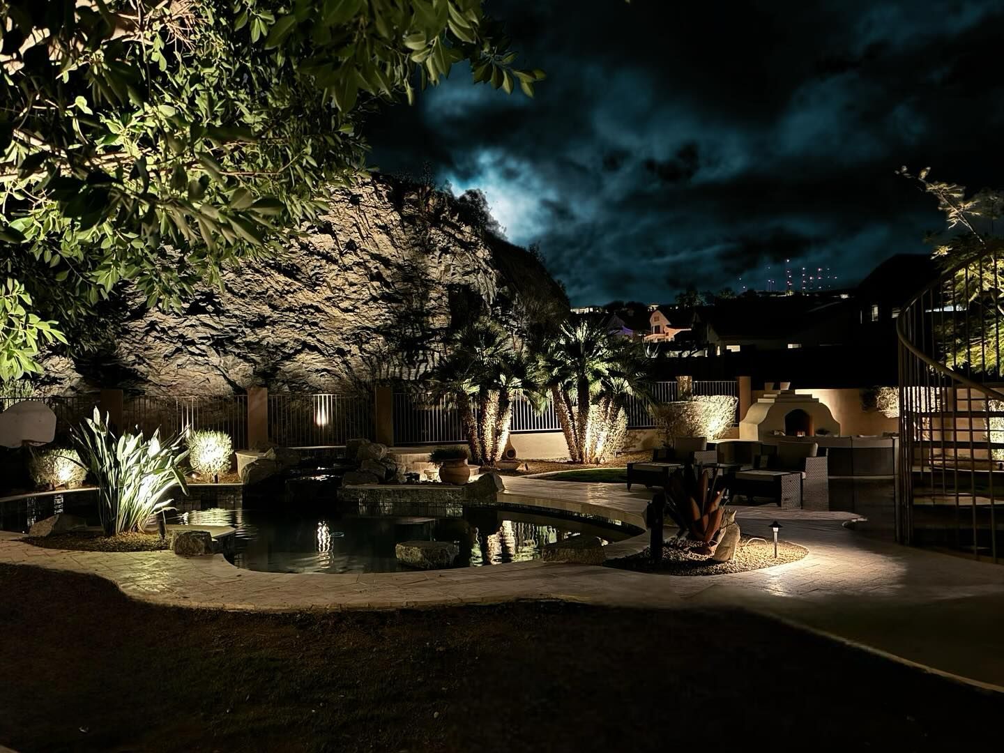 Nighttime resort courtyard with palm trees, stone walls, and lit pathways around a pool
