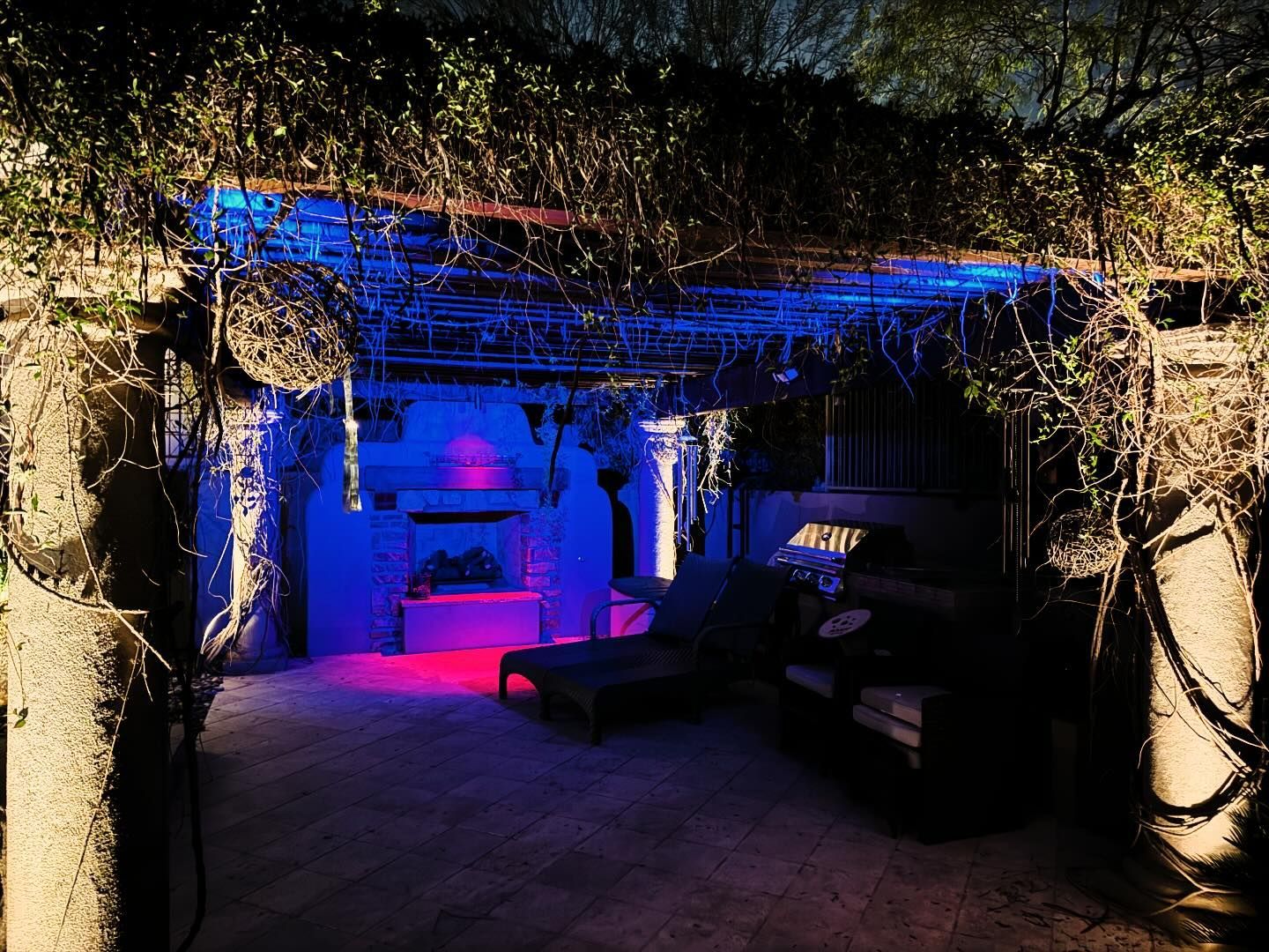 Lit patio lounge with blue-purple lighting, vine-covered archway, and outdoor seating at night
