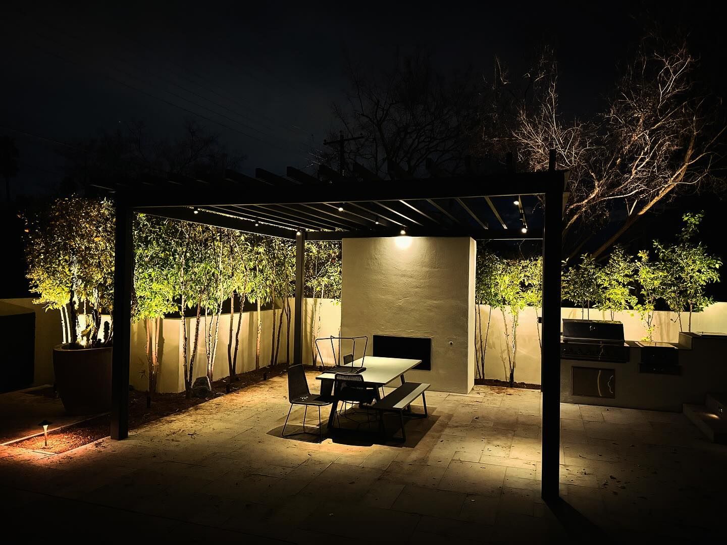 Nighttime patio with pergola, dining table, and warm garden lighting in a backyard