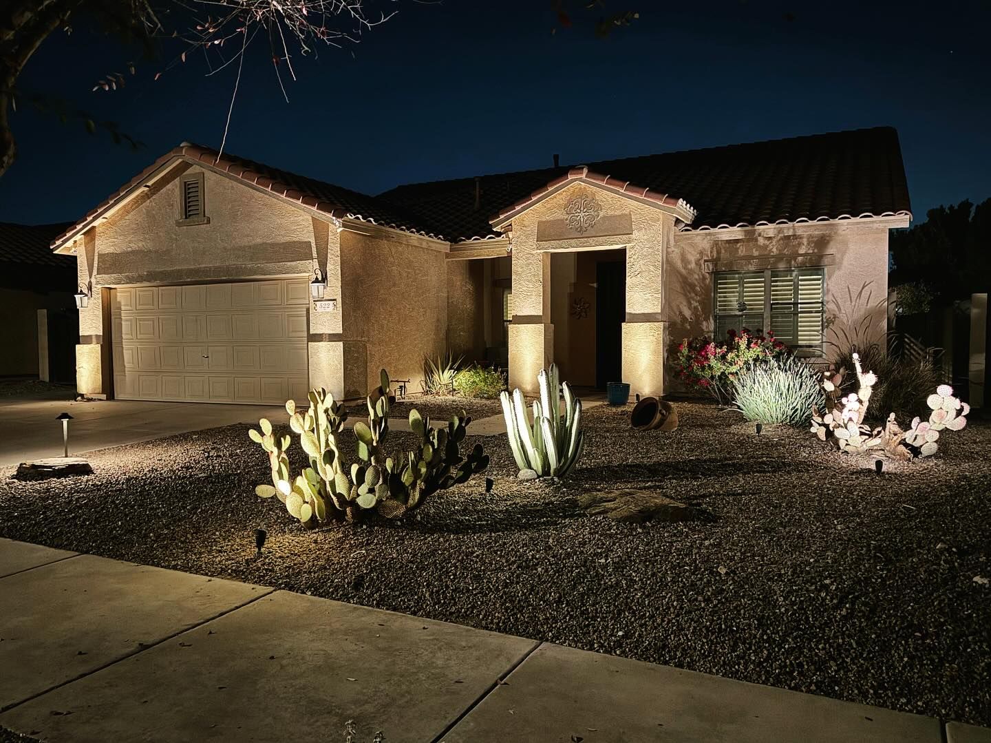 Nighttime view of a lit suburban house with fireworks overhead and desert landscaping in front