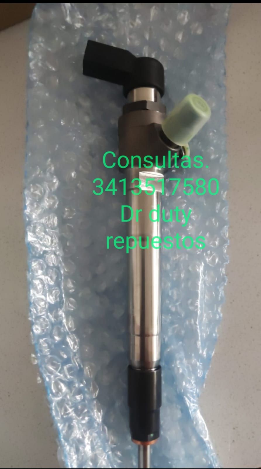 Inyector de combustible con componentes verdes y negros, apoyado sobre plástico de burbujas azul.