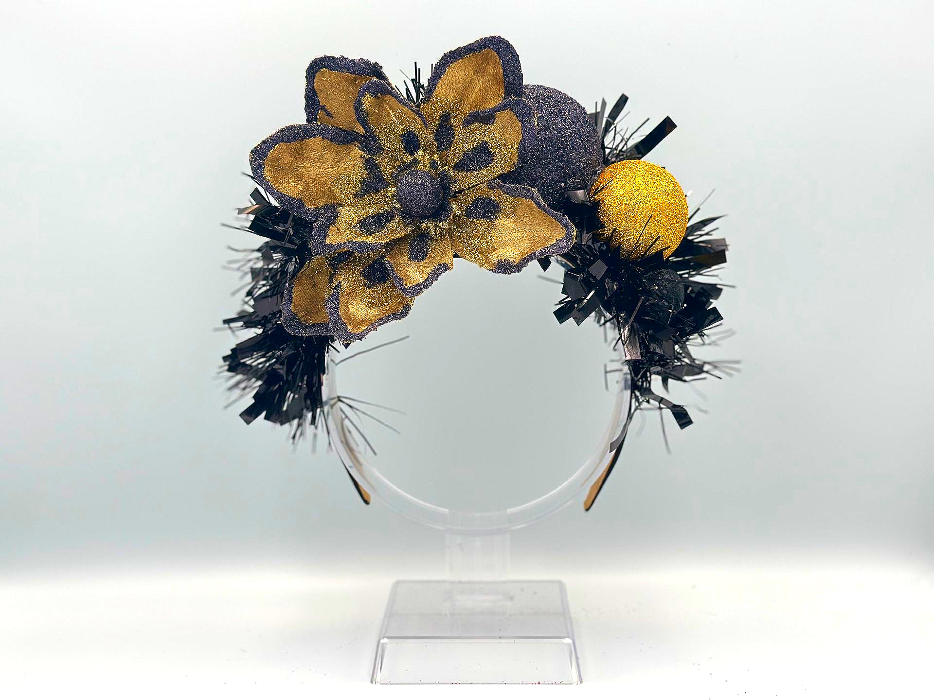 A headband decorated with a large gold glittered flower, a black glittered sphere, and a smaller gold textured orb.