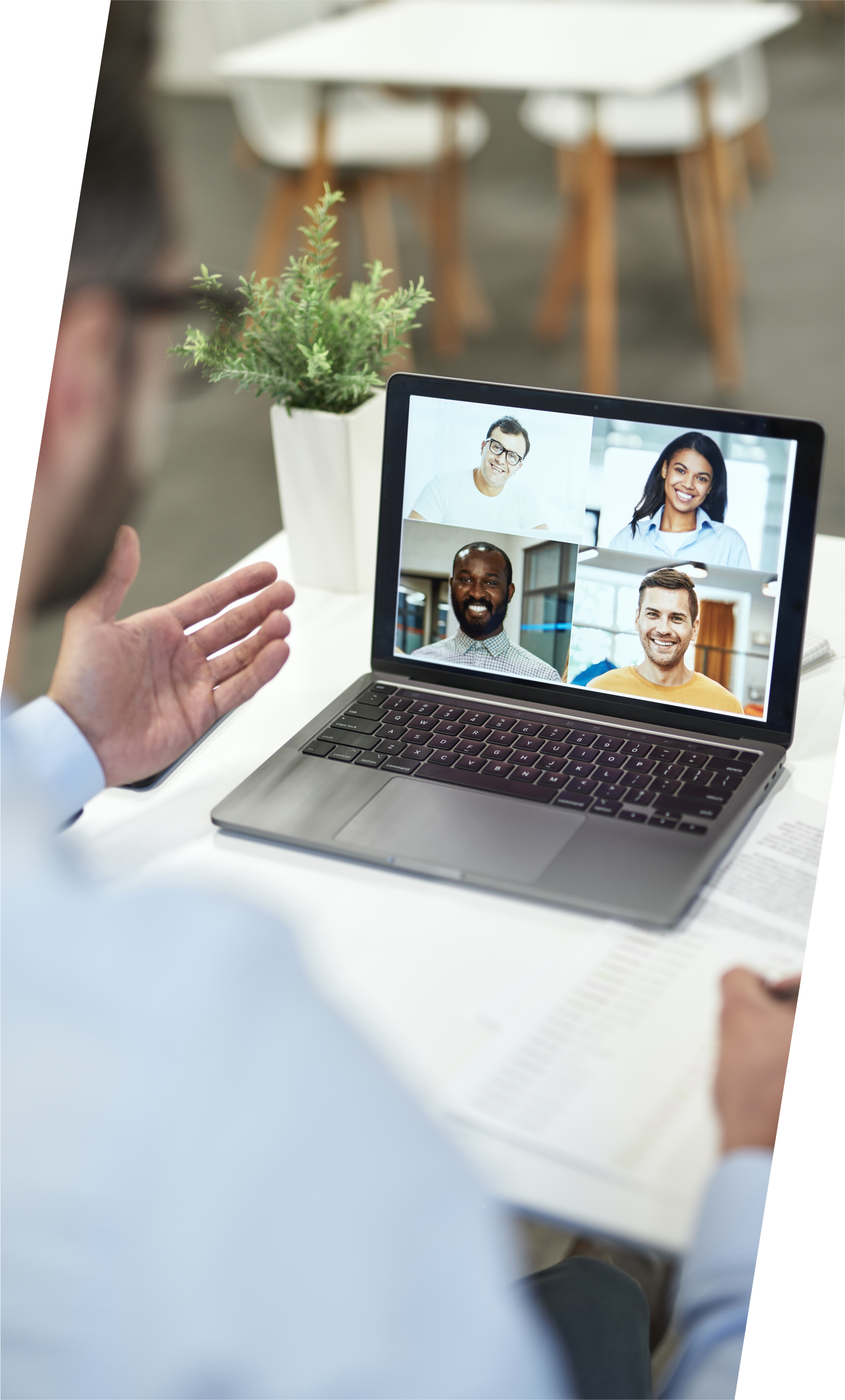 Person in light blue shirt on a video call with 4 people; a laptop is on a white desk with a plant.