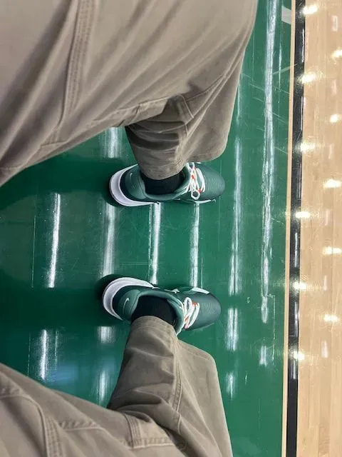 A person is standing on a basketball court wearing green shoes.