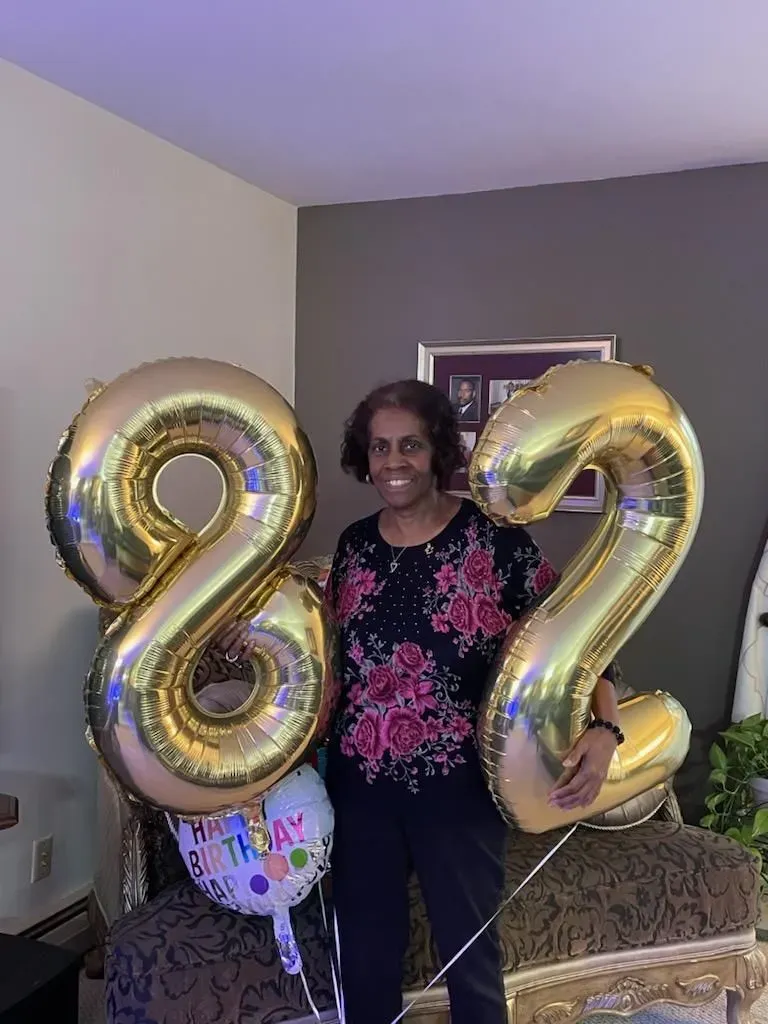 A woman is holding balloons in the shape of the number 82.