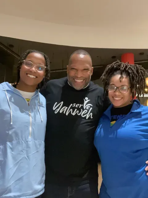 A man and two women are posing for a picture and the man is wearing a shirt that says yahwen