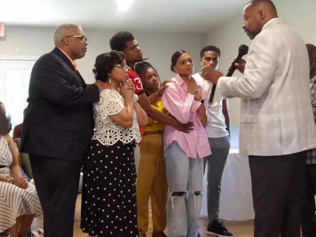 A group of people are standing around a man holding a microphone.