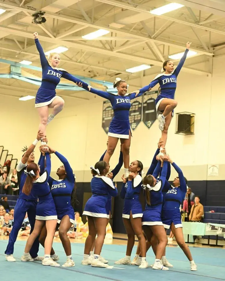 A group of cheerleaders are performing in a gym wearing dms uniforms