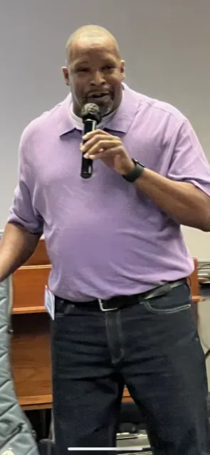 A man in a purple shirt is holding a microphone.