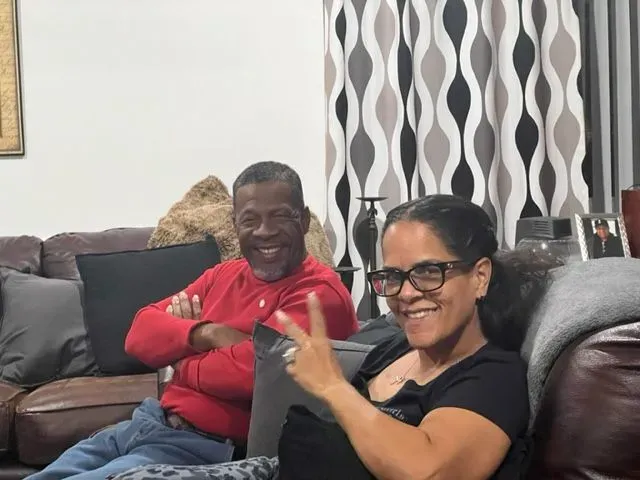A man and a woman are sitting on a couch and the woman is giving a peace sign