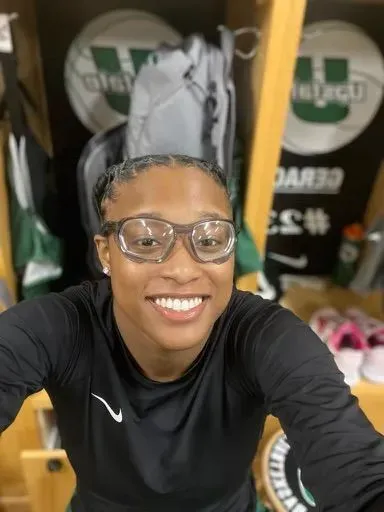 A woman wearing glasses is smiling in a locker room.
