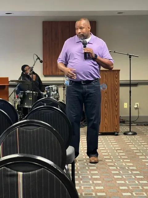 A man in a purple shirt is speaking into a microphone