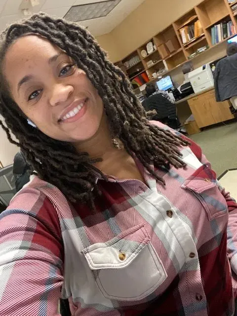 A woman with dreadlocks is smiling and wearing a plaid shirt