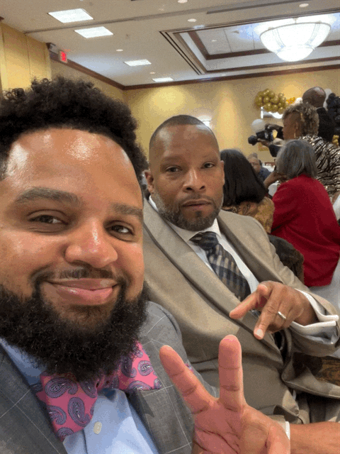 Two men in suits and bow ties are taking a selfie in a room.