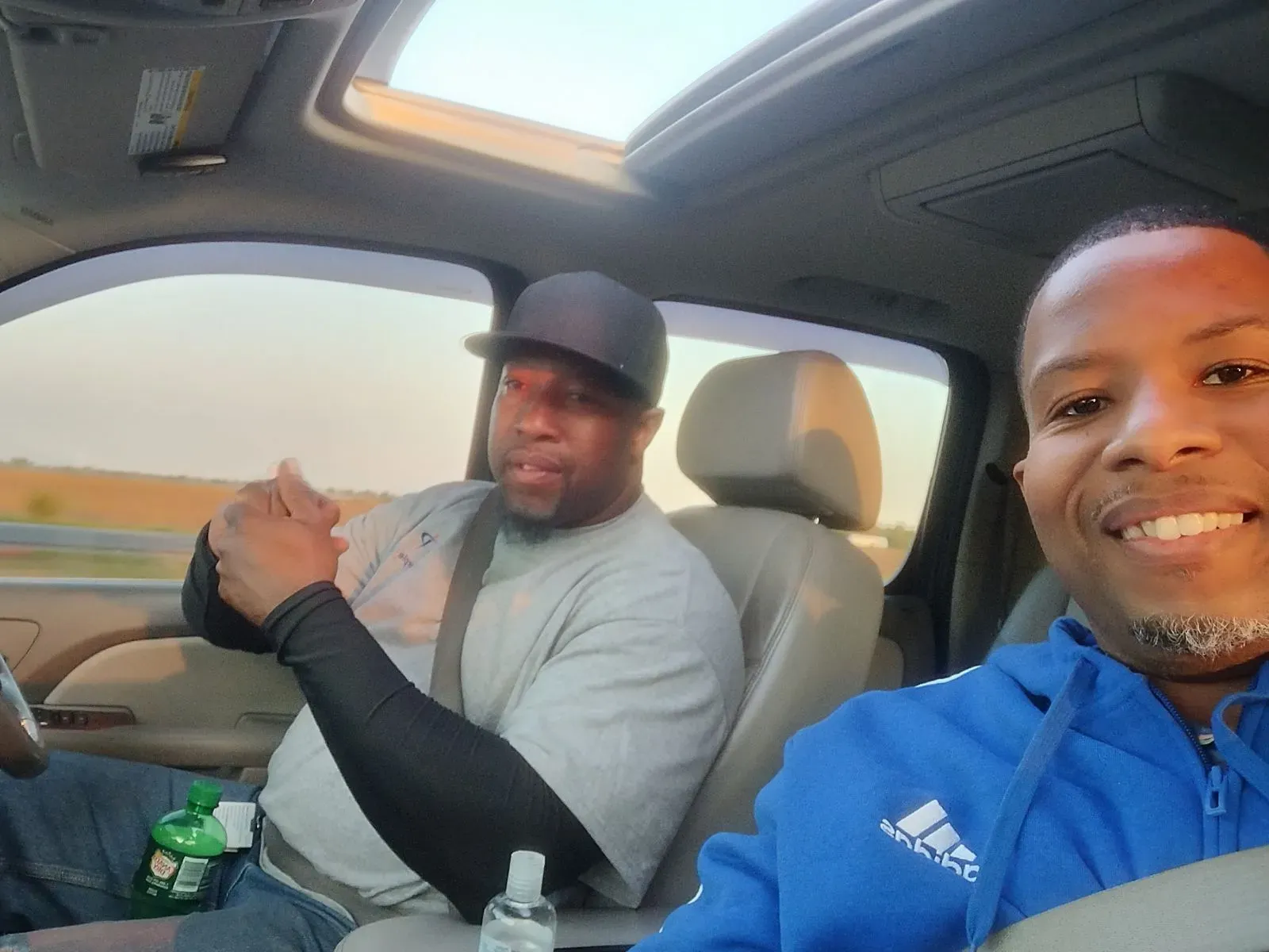 Two men are sitting in a car and one is wearing an adidas jacket