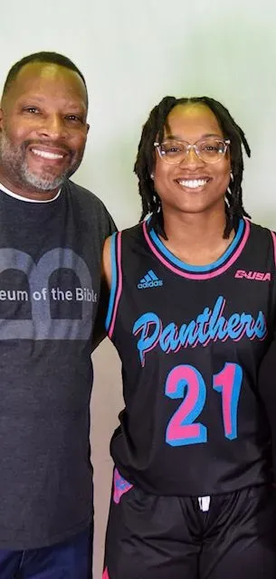 A man and a woman are posing for a picture . the woman is wearing a panthers jersey.