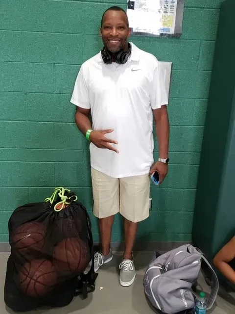 A man wearing headphones is standing next to a bag of basketballs