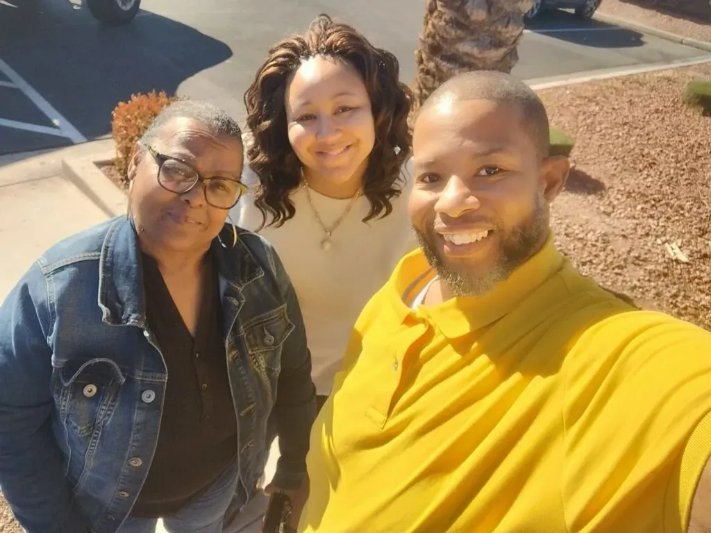 A man in a yellow shirt is posing for a picture with two women.