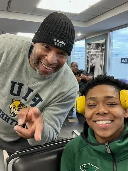 A man wearing a sweater that says u13 is standing next to a boy wearing yellow headphones