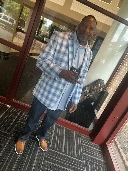 A man in a plaid jacket is standing in front of a glass door.