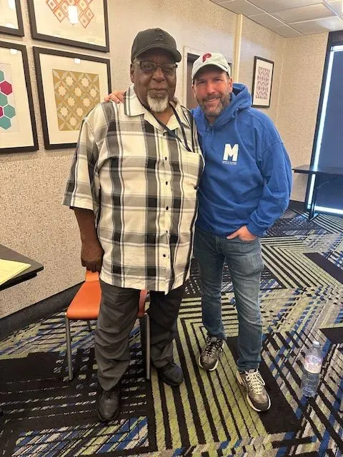 A man in a blue hoodie with the letter h on it poses for a picture with another man
