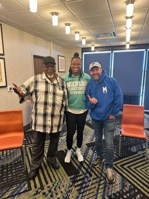 Two men and a woman are posing for a picture in a room with chairs.