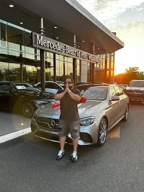 A man is standing in front of a mercedes benz dealership