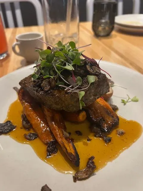 A white plate topped with a piece of meat and carrots