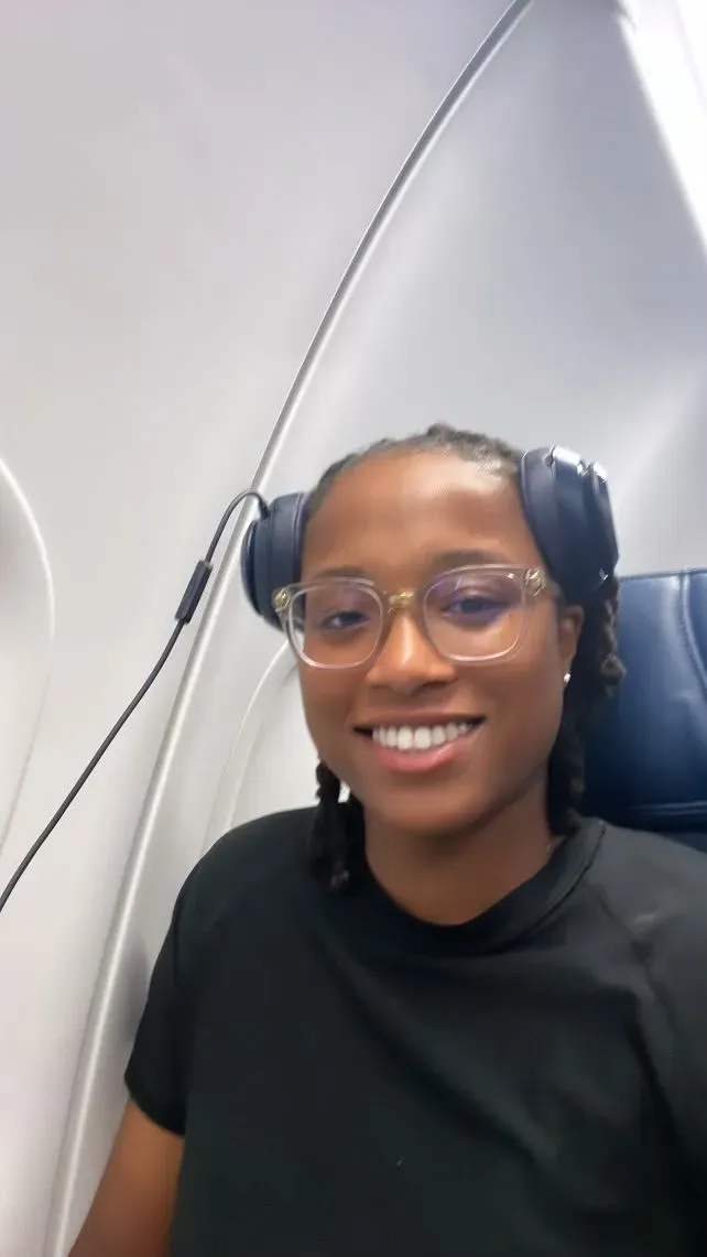 A woman wearing glasses and headphones is sitting on an airplane.