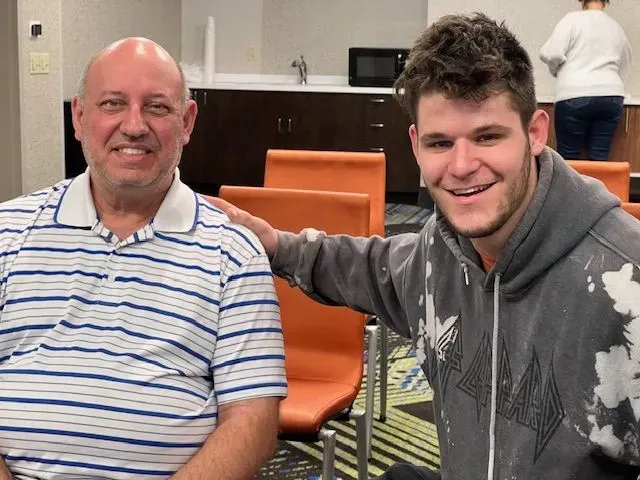 Two men are posing for a picture in a room with orange chairs.