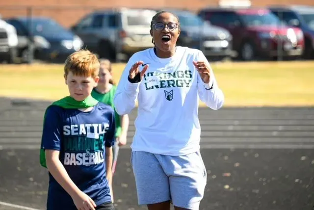 A woman wearing a seattle baseball shirt is talking to a boy wearing a green shirt.