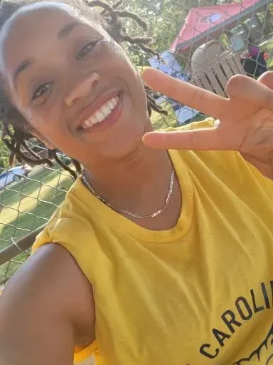 A woman in a yellow shirt is giving a peace sign.